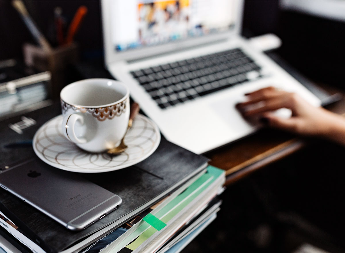 A person is sitting at a desk with a laptop and coffee.